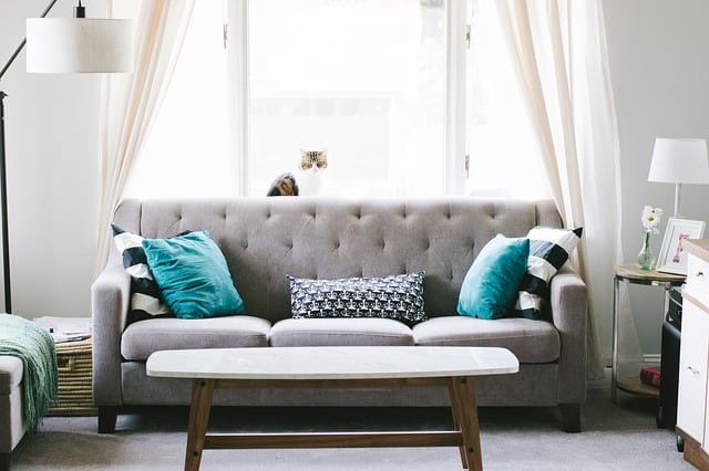 Tidy living room after home declutter with grey decor and couch with turquoise pillows in front of window.