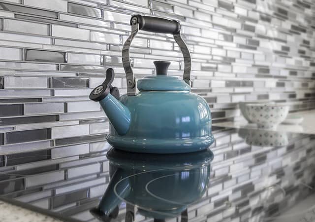 Clutter-free kitchen stovetop with grey tile backsplash and turquoise teakettle.