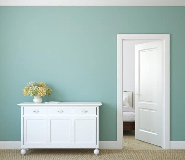 white sideboard with flowers in vase against aqua wall with white trim and door partially open to bedroom