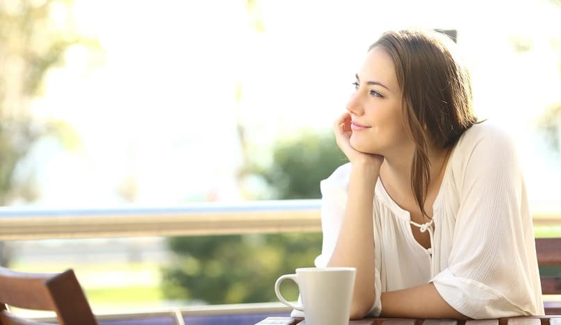 Happy woman sitting outdoors on a sunny morning with a coffee mug.