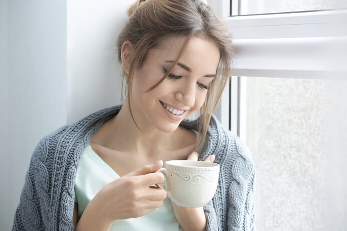 happy woman wearing gray sweater drinking from a white mug