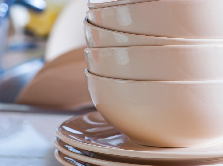 stacked white dishes on kitchen counter with cluttered sink in background