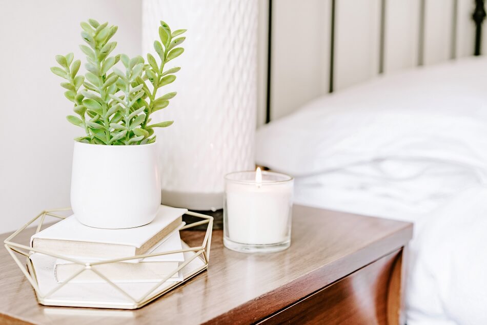 white clutter-free bedroom with table, books, plant, candle, lamp