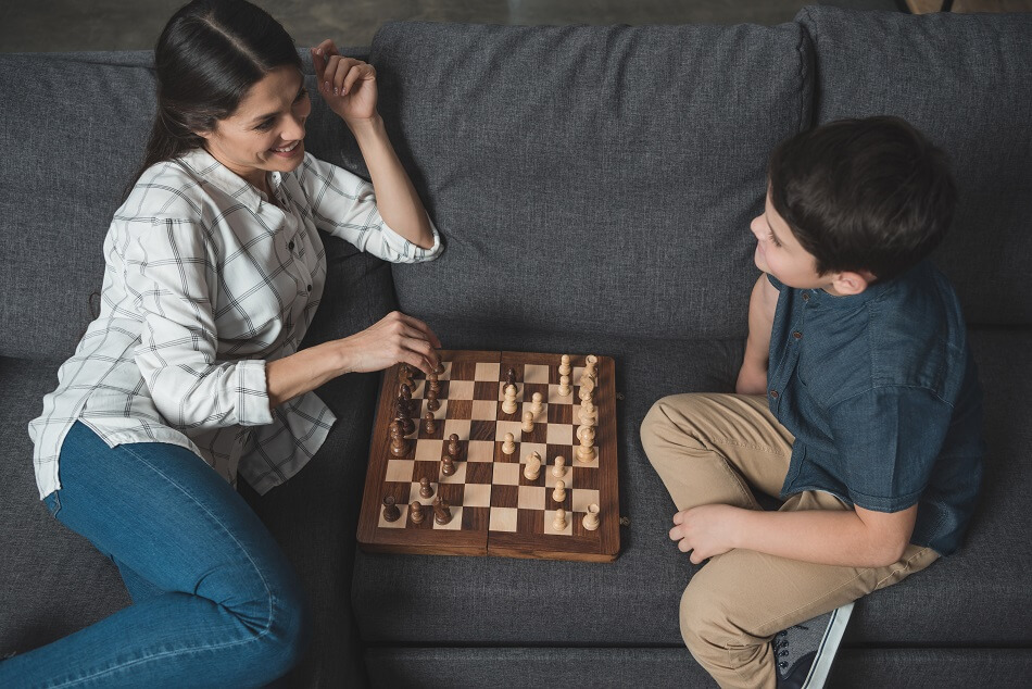 mother and son sitting on dark gray couch and playing chess to build positive relationship