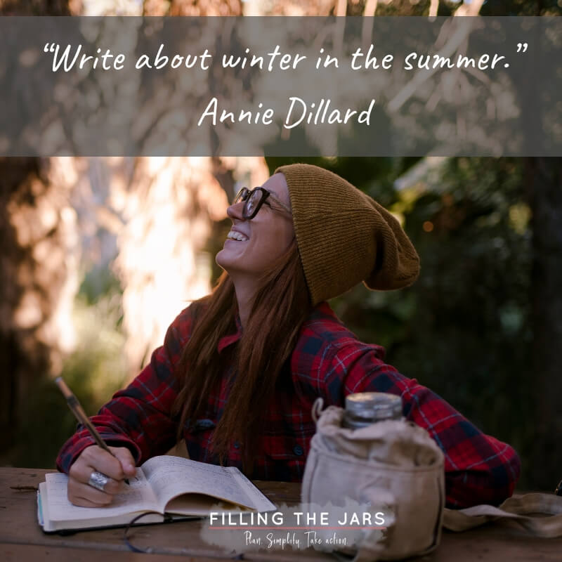 Woman wearing red plaid shirt glasses and knit hat writing in journal in rustic woods setting.