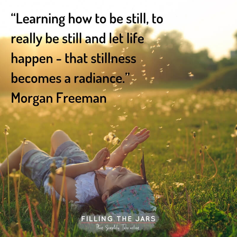 Child lying in grass during summer blowing dandelion seeds with text overlay quote morgan freeman stillness becomes radiance.