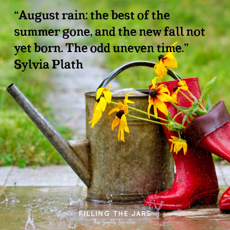 Watering can and red boots on sidewalk during summer rain with text overlay quote sylvia plath august rain odd uneven time.