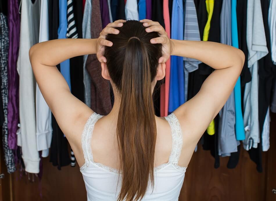 overwhelmed woman with long dark ponytail in front of wardrobe that needs to be decluttered