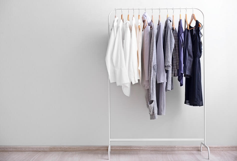 simple decluttered wardrobe in neutral tones hanging on white clothing rack against white wall