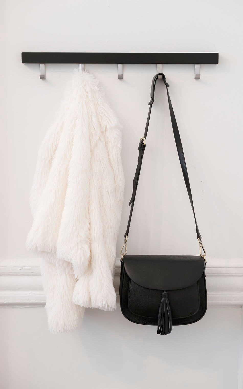 white jacket and black purse hanging against white wall