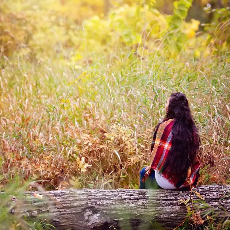 woman sitting on log in autumn forest thinking about goals to set for next year