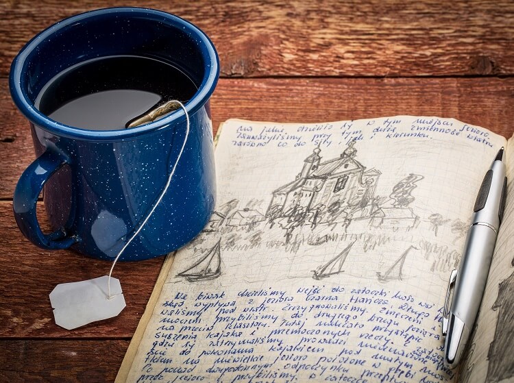 wood table with tea in blue mug and journal with doodles and response to writing prompt