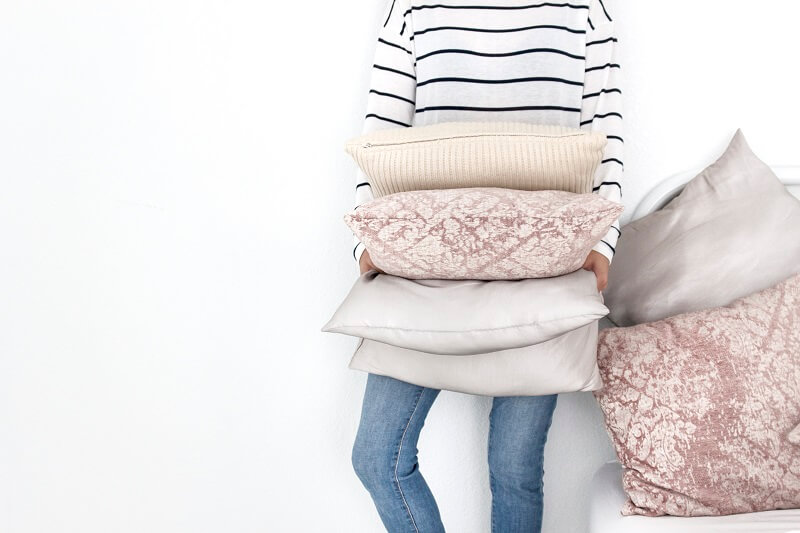 woman in striped sweater and jeans against white background getting ready to declutter extra pillows