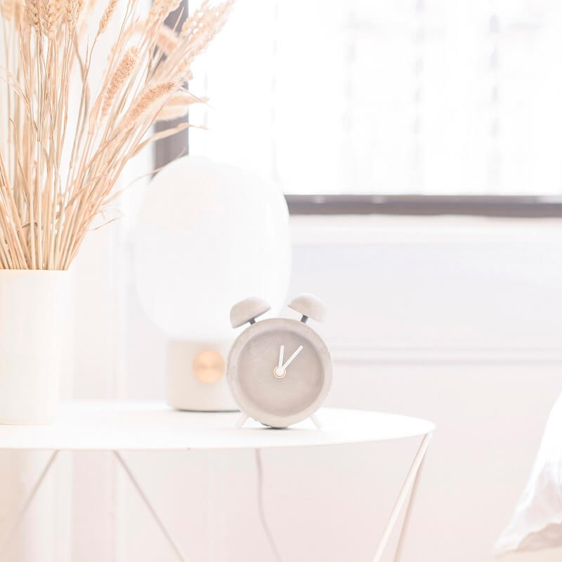 clock lamp and vase of wheat on white table with morning light streaming through bedroom window