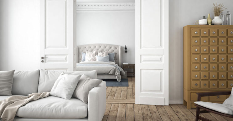 comfortable and uncluttered white living room with view into tidy bedroom with wood floors