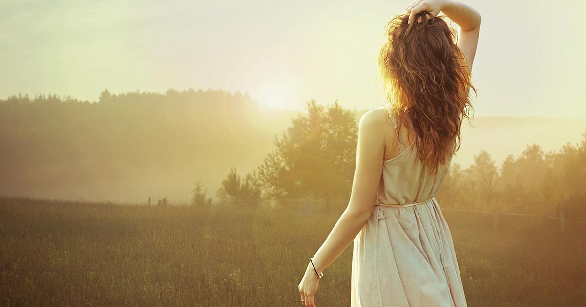 woman with long dark hair and casual white dress watching inspirational summer morning sunrise