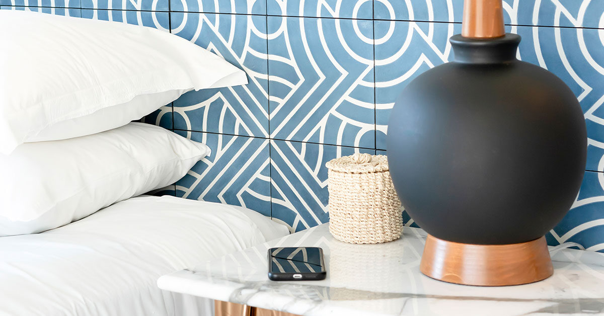 white pillows on bed and black lamp with phone on bedside table against blue patterned wall