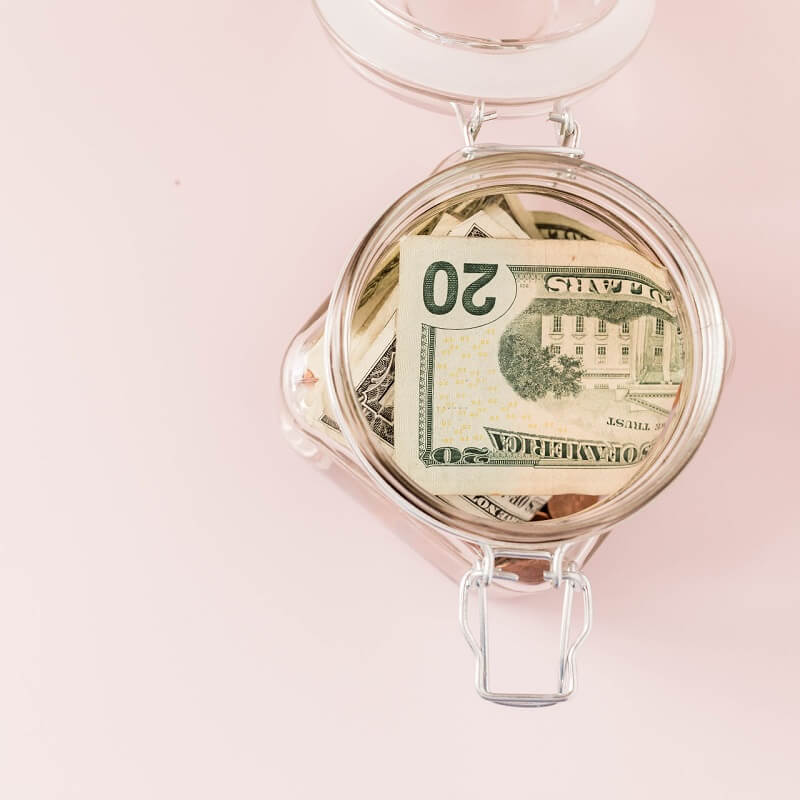 pink background with glass jar of money saved during no spend month