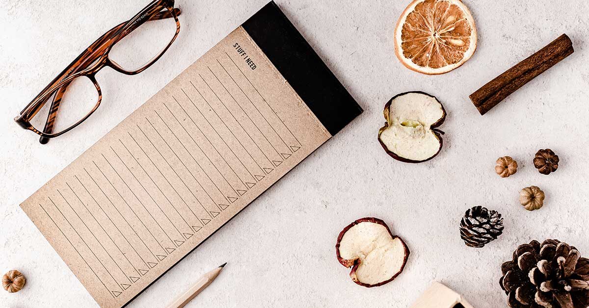 flatlay with reading glasses notepad pencil dried fruit and nuts on mottled white background