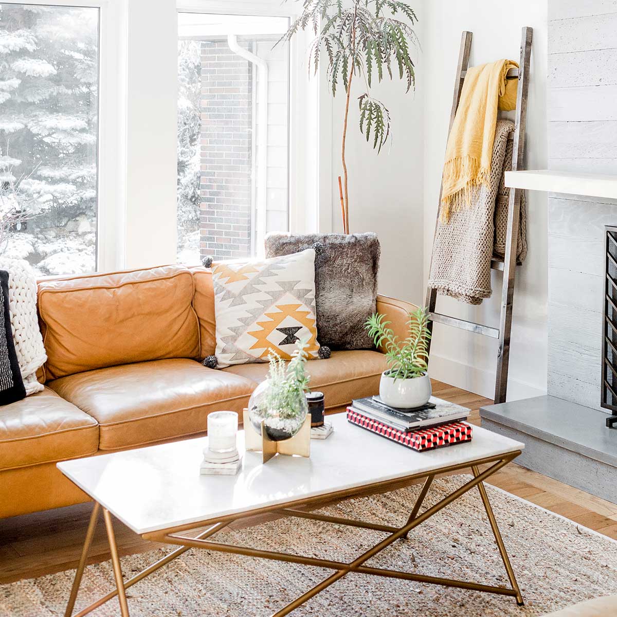 clutter-free white living room with modern coffee table and brown leather couch with cozy pillows and throws