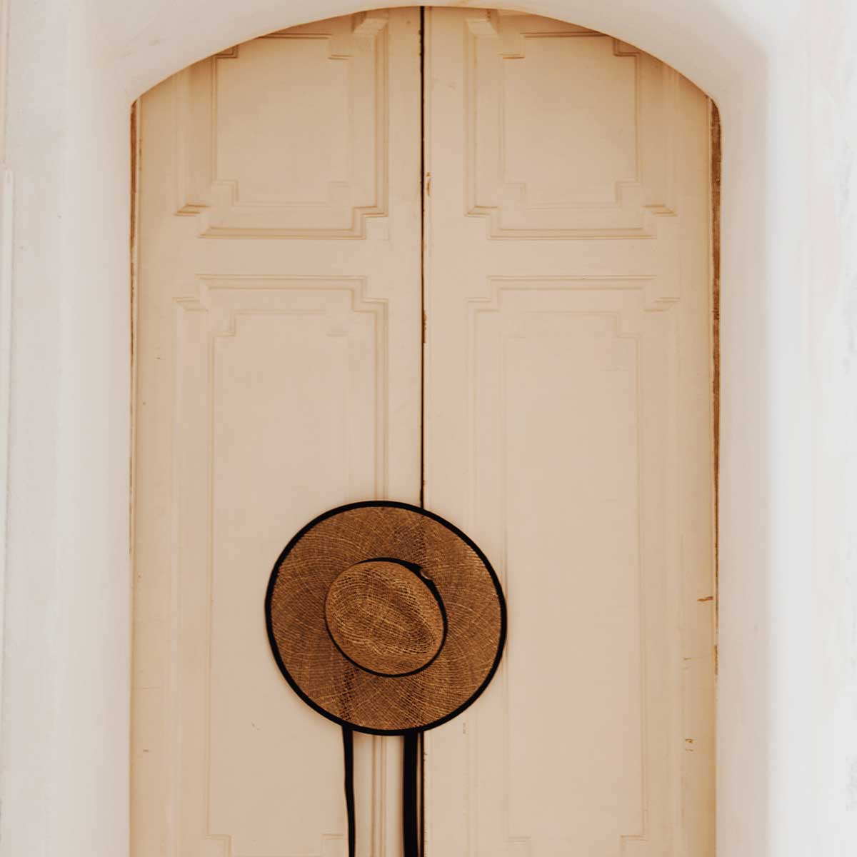 painted raised panel double door set behind white walls with straw hat hanging on handle