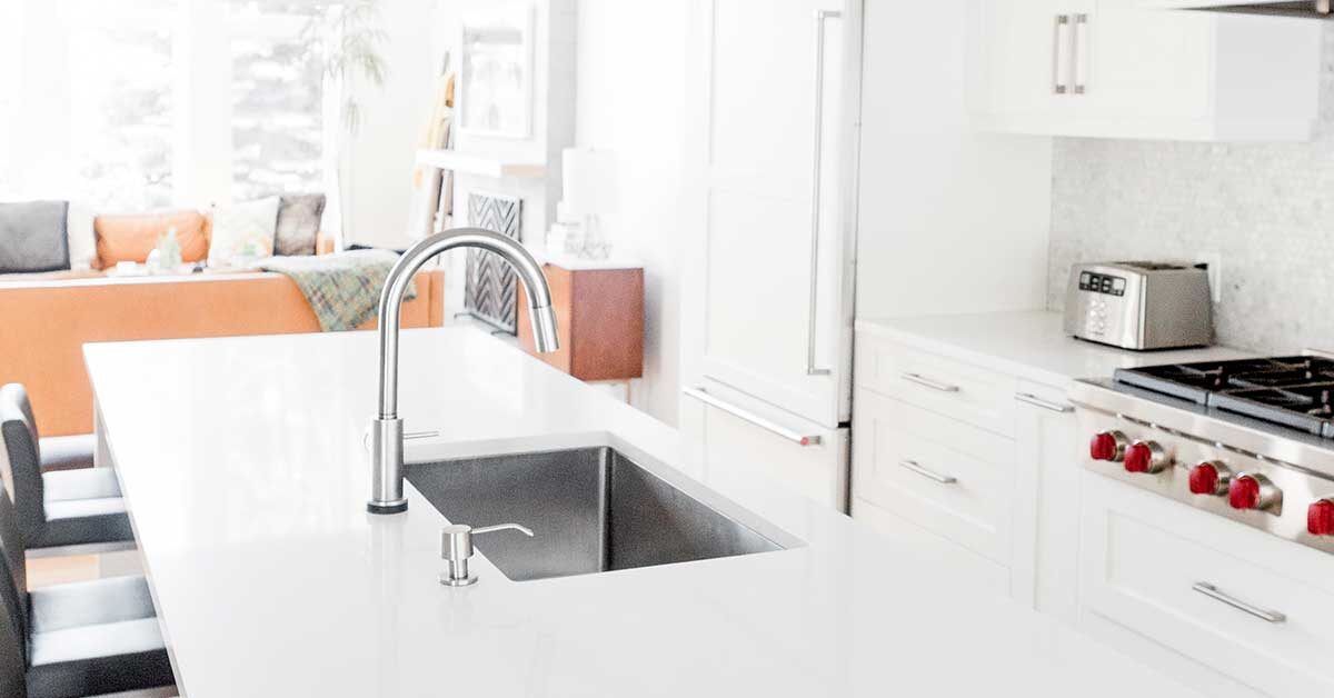 clean and decluttered white kitchen with stainless accents and black barstools with comfortable living room in background