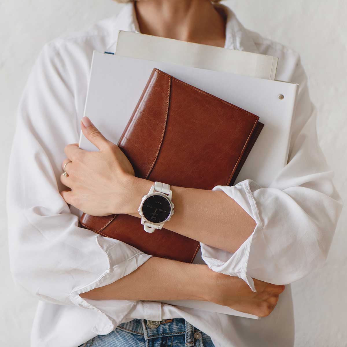 woman wearing white watch and white shirt holding leather journal and white binders