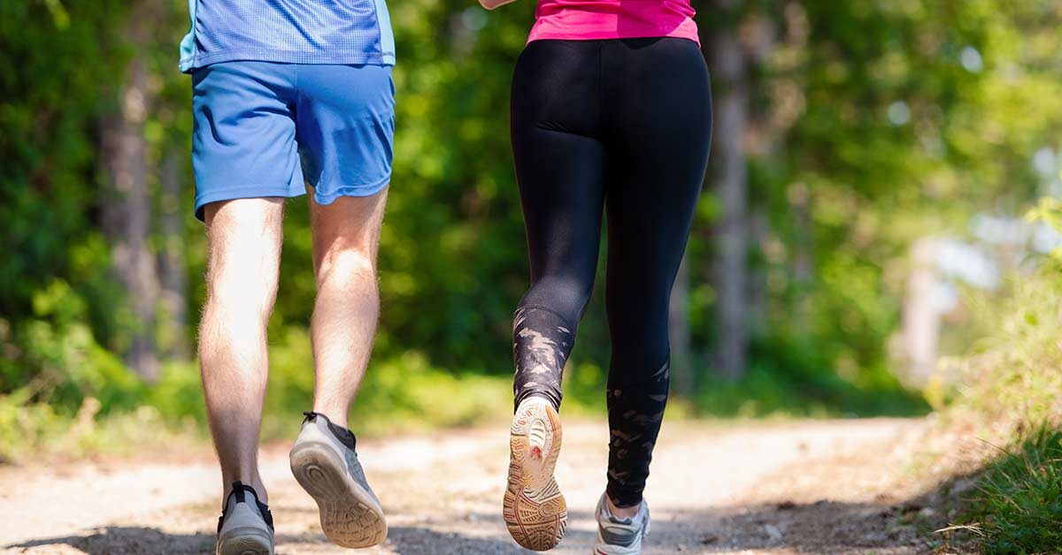 man and woman running on sunny dirt trail