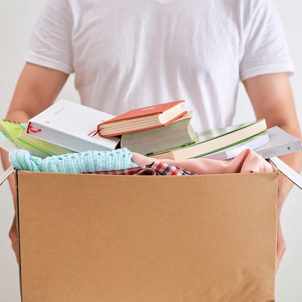 Man in white t-shirt holding cardboard box of decluttered items.