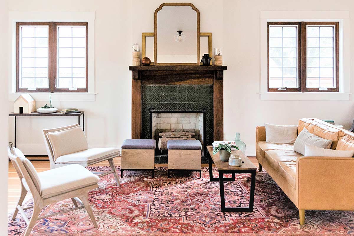 Clutter-free and simple living room with white walls, fireplace, and simple comfortable furniture on red patterned rug.