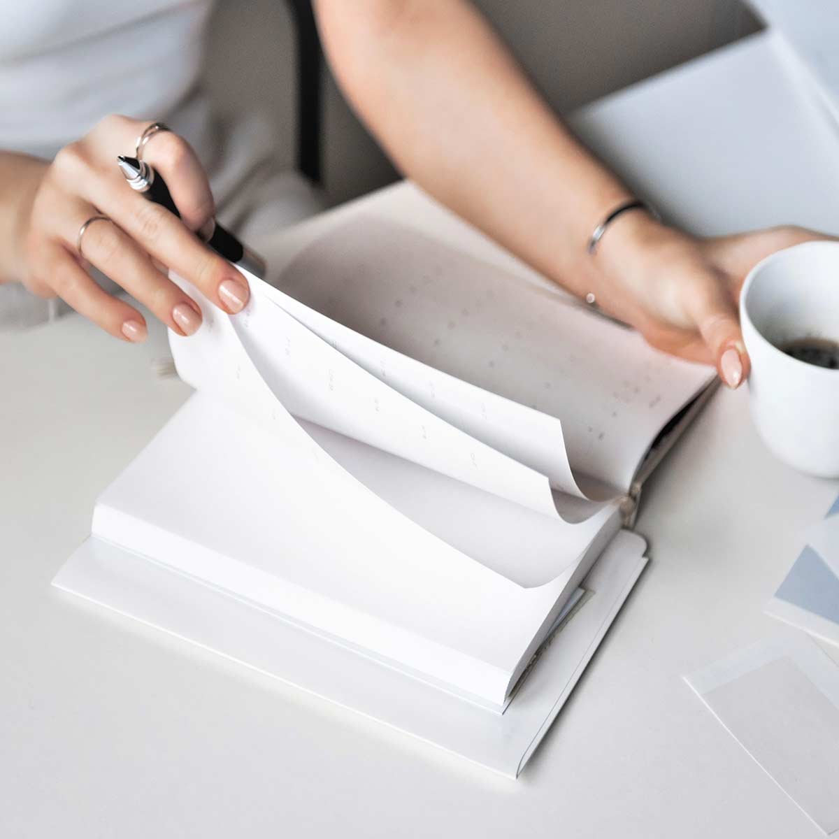 Adult woman sitting at white desk holding coffee cup while preparing to do daily journaling.