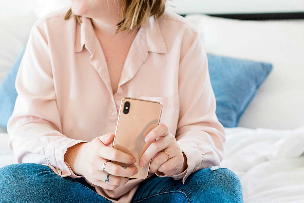 Woman in pink blouse and jeans sitting down while holding pink phone.