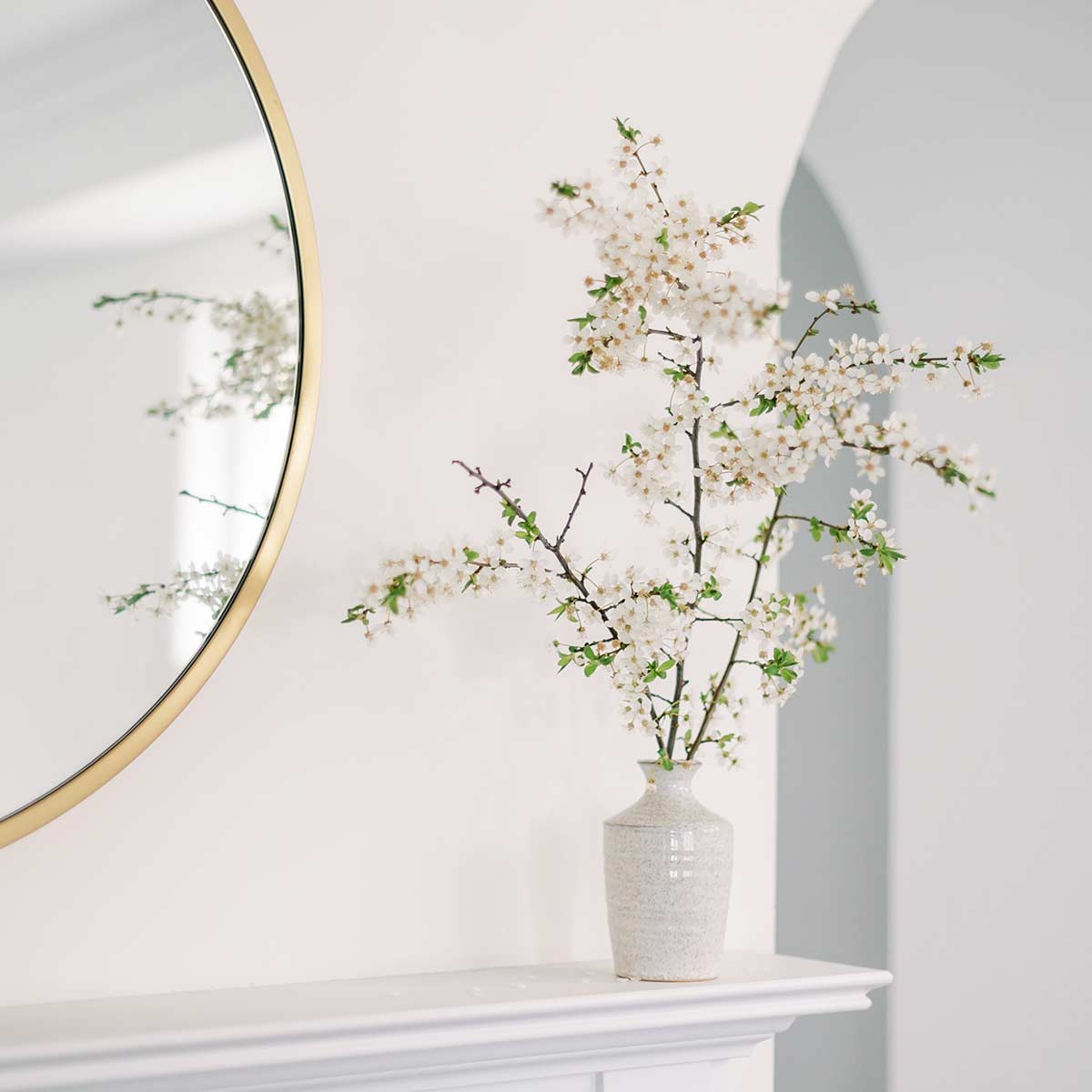 Spring flowering branch in white vase on clutter-free white mantel.