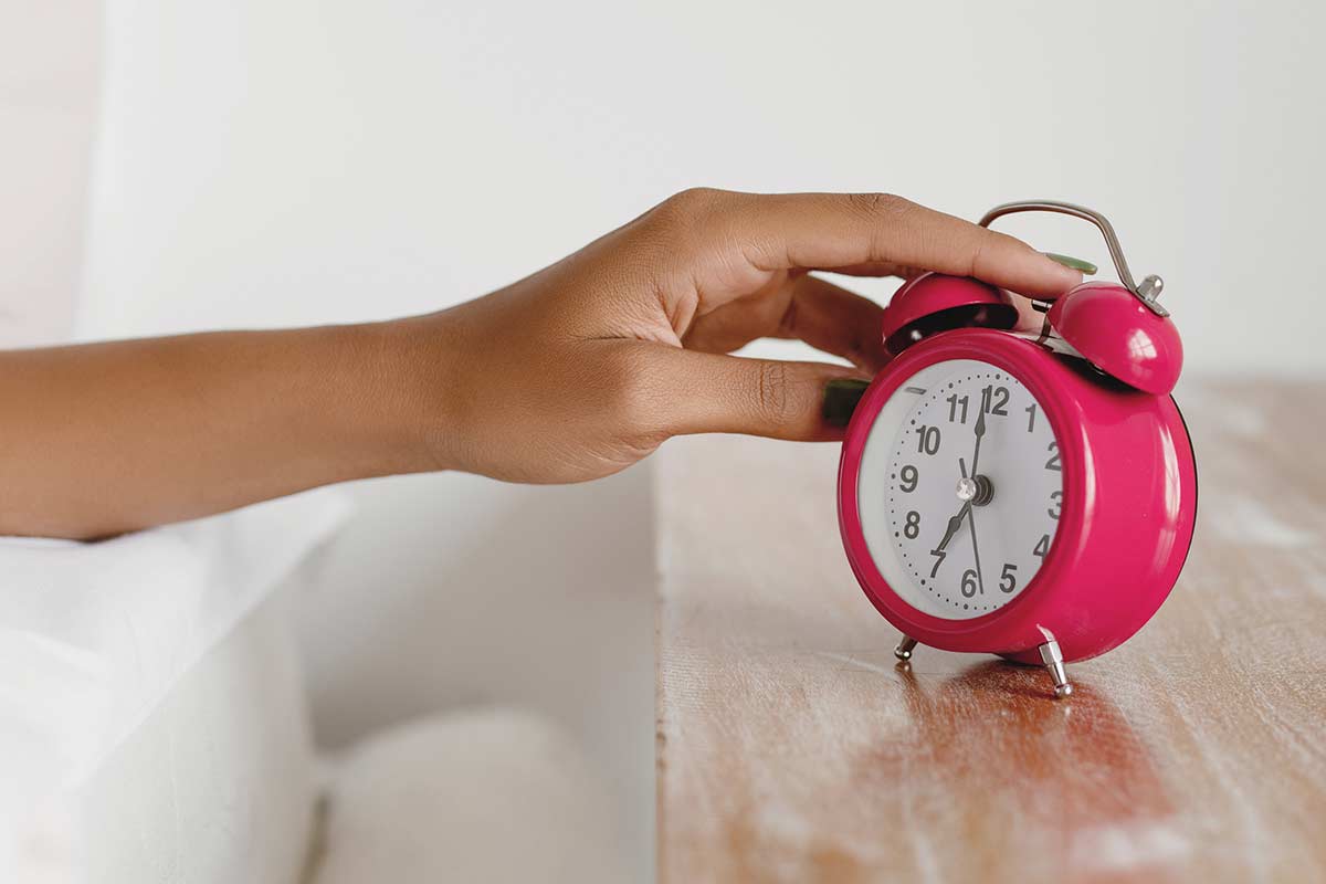 Woman's hand reaching to turn off the alarm on pink clock.