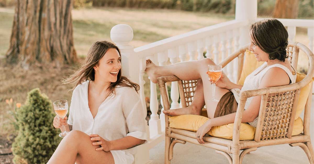 Two women laughing and sitting on a porch.