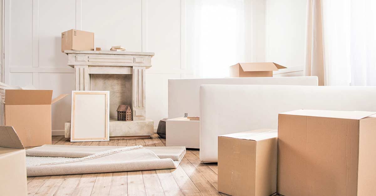 White living room with packing boxes and miscellaneous decor scattered over rustic wood floor.