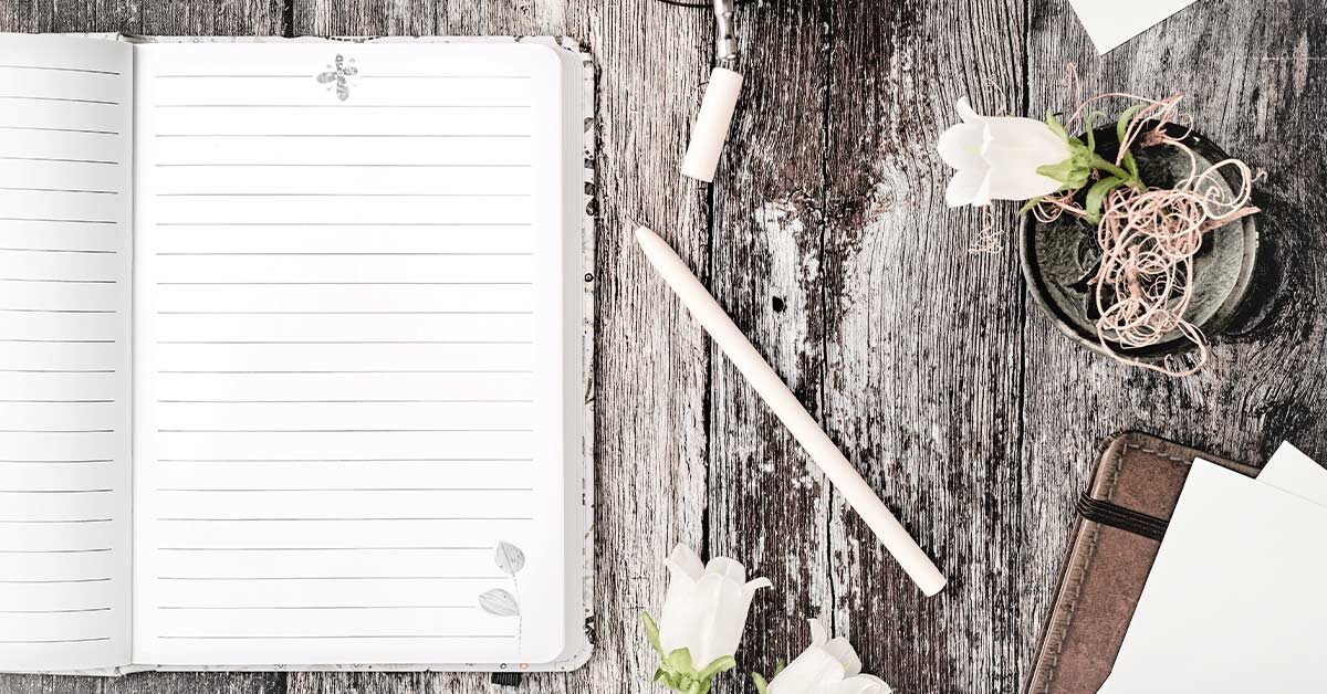 Open lined journal on rustic wood table with pen and flowers and leather journal.