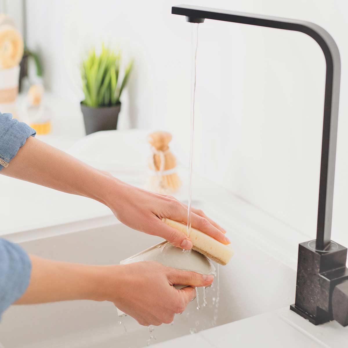 Female hands washing dish in white sink with modern black faucet.