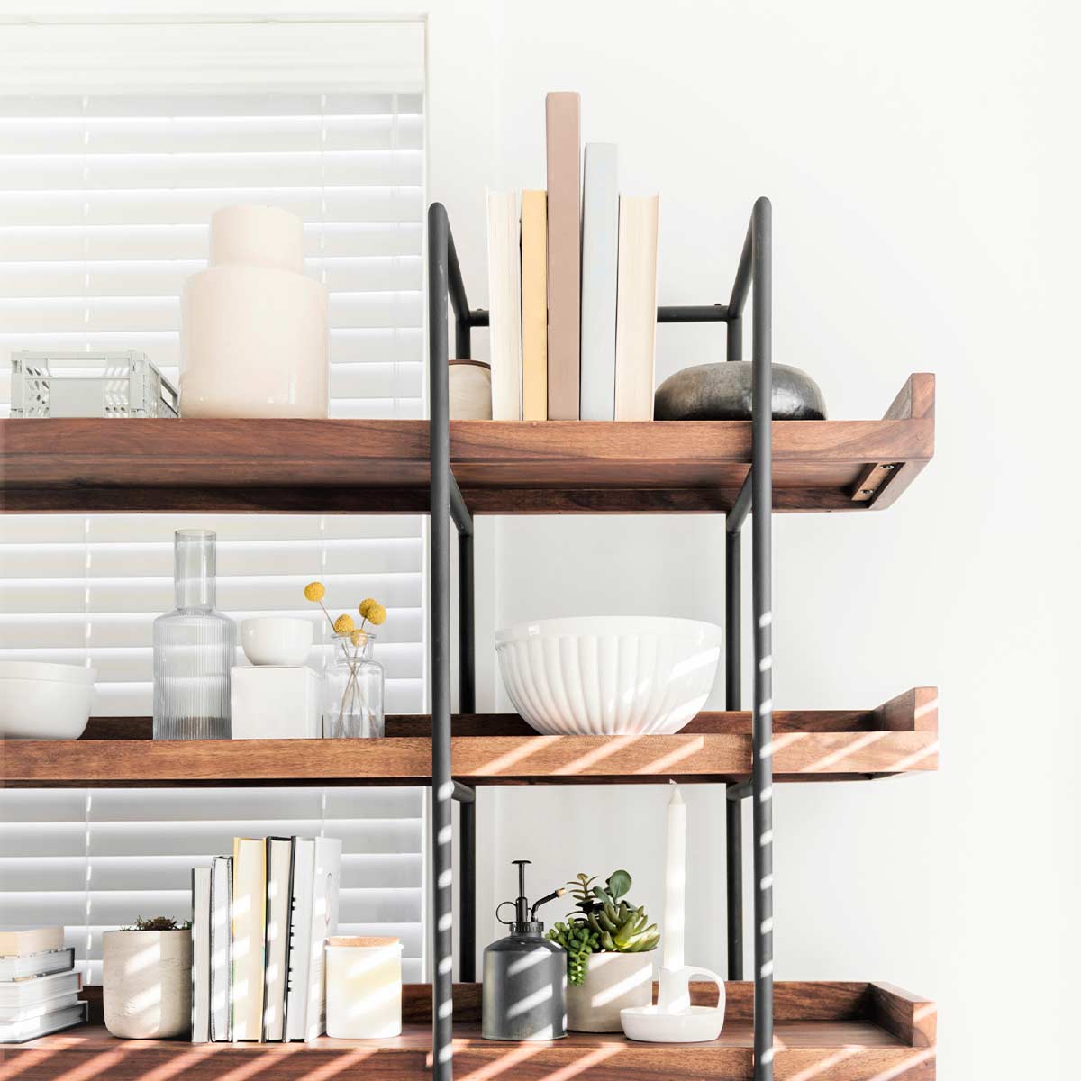 Carefully chosen white and neutral decor items on wood and iron shelves in front of white wall.