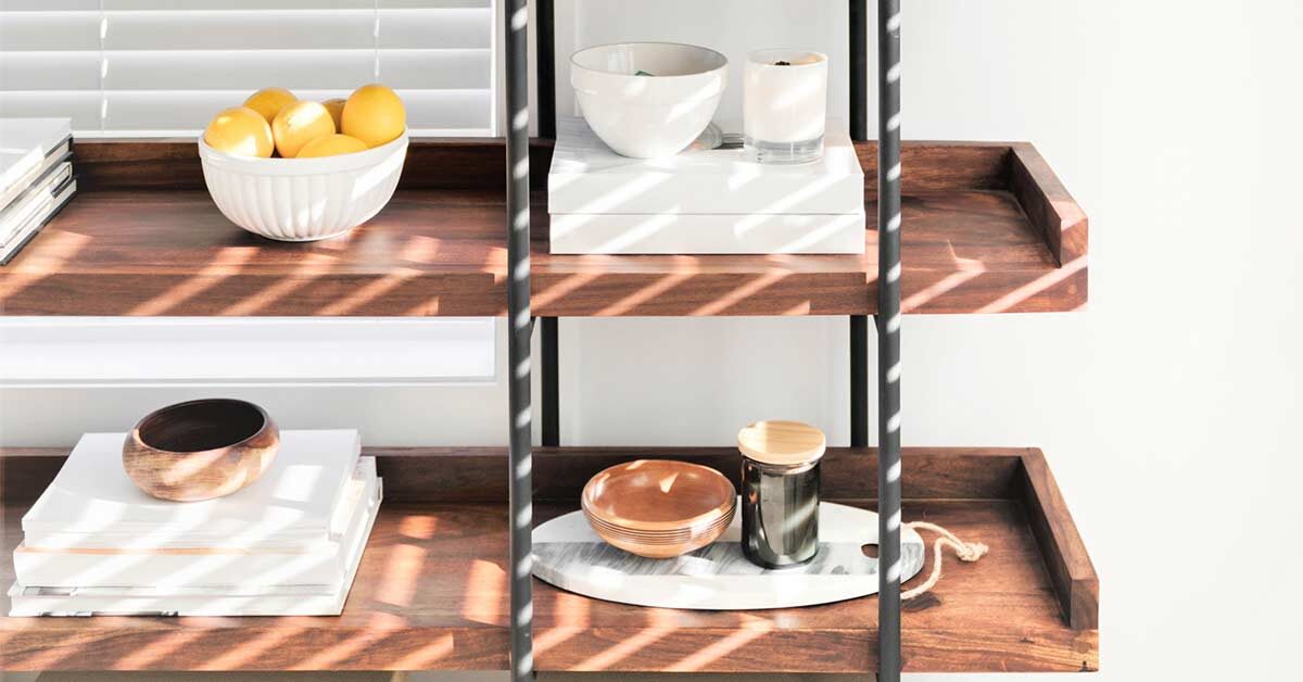 Carefully chosen white and neutral decor items on wood and iron shelves in front of white wall.