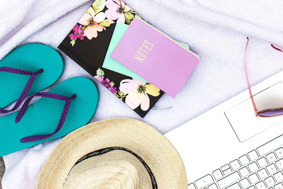 Items necessary to be productive during the summer at the pool - laptop, sunglasses, straw hat, flip-flops, planner, notebook.