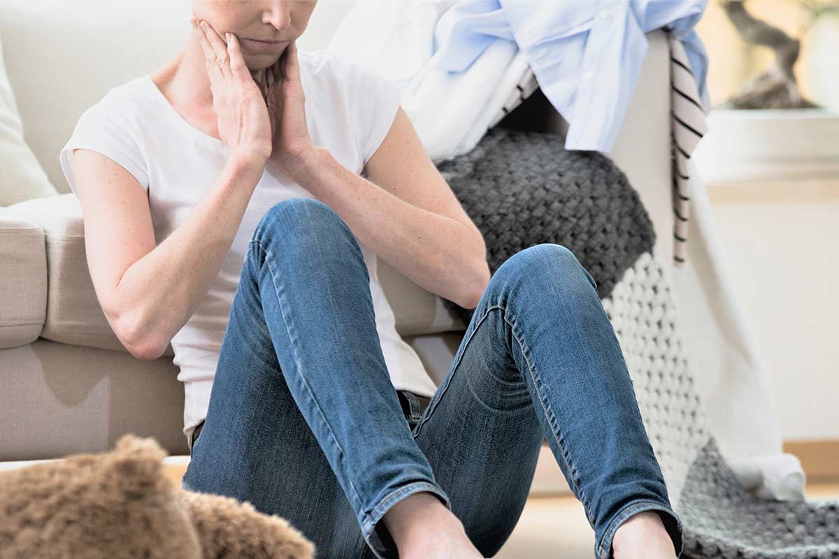 Woman sitting on floor feeling overwhelmed by cluttered house.