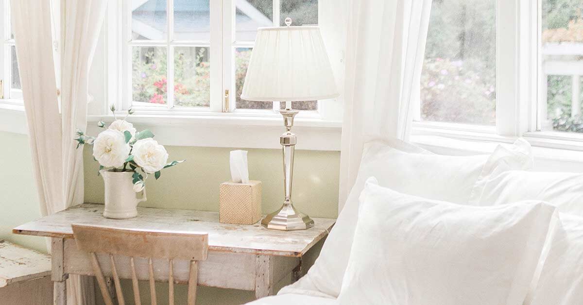 Clutter-free bright and airy bedroom with white linens and rustic desk.