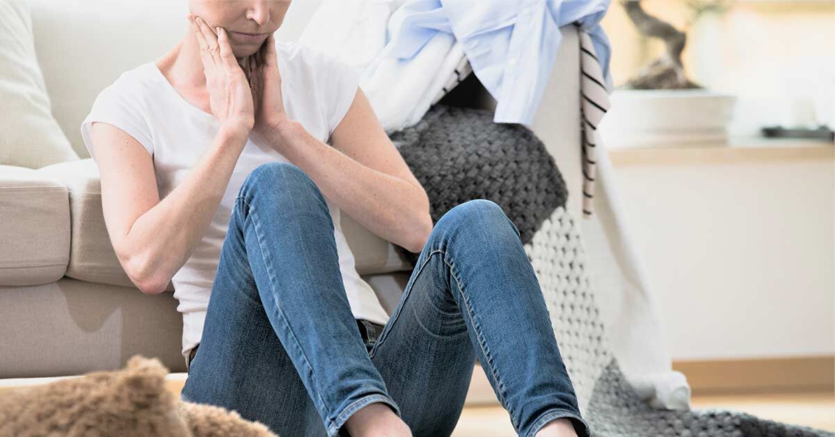 Woman sitting on floor feeling overwhelmed by cluttered house.
