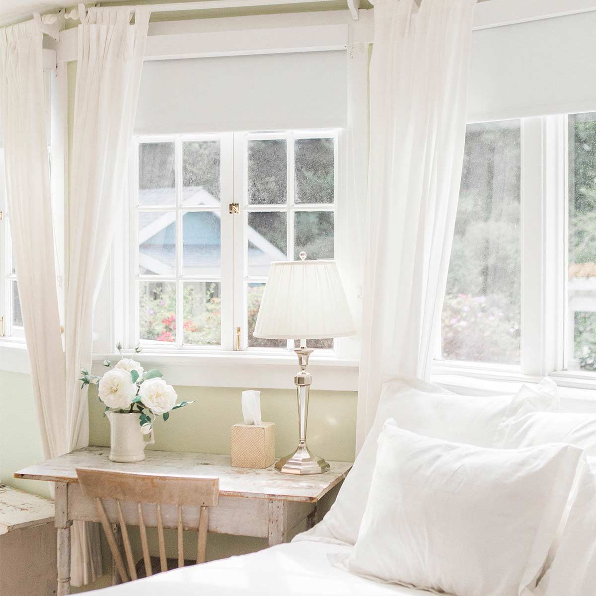 Clutter-free bright and airy bedroom with white linens and rustic desk.