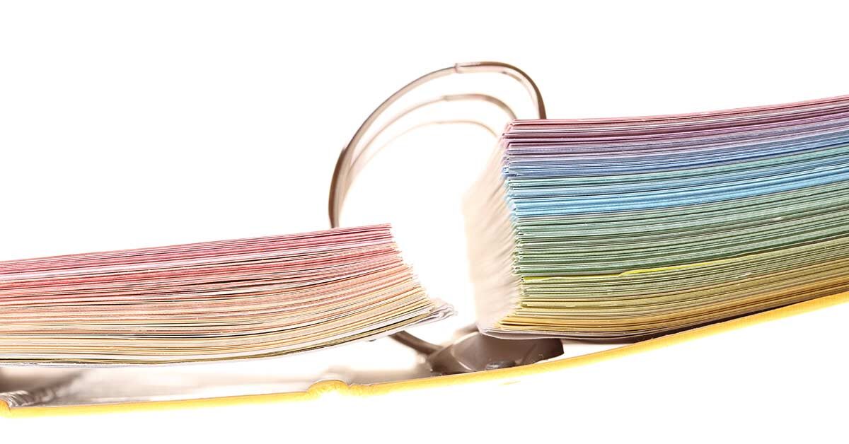 End view of open 3 ring binder with colorful pages on white background.