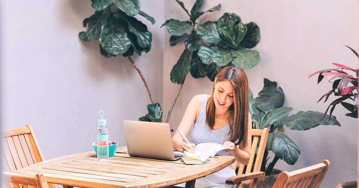 Woman sitting at wood folding table and writing responses to creative journal prompts.