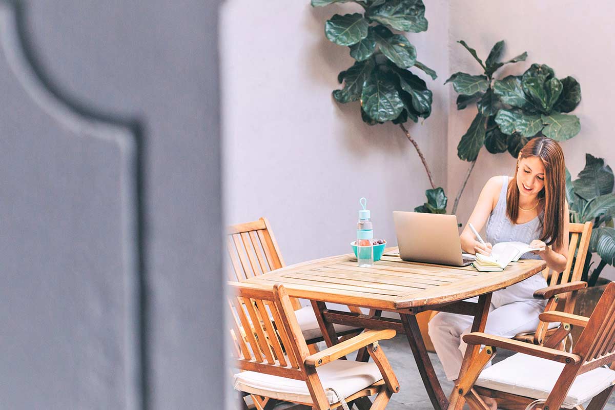 Woman sitting at wood folding table and writing responses to creative journal prompts.