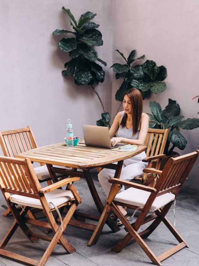 Woman sitting at table and journaling on her laptop outdoors.