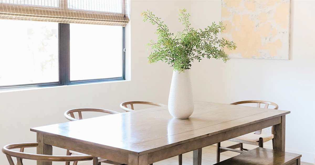 Clutter-free dining table with white vase and greenery in sunny white dining room.